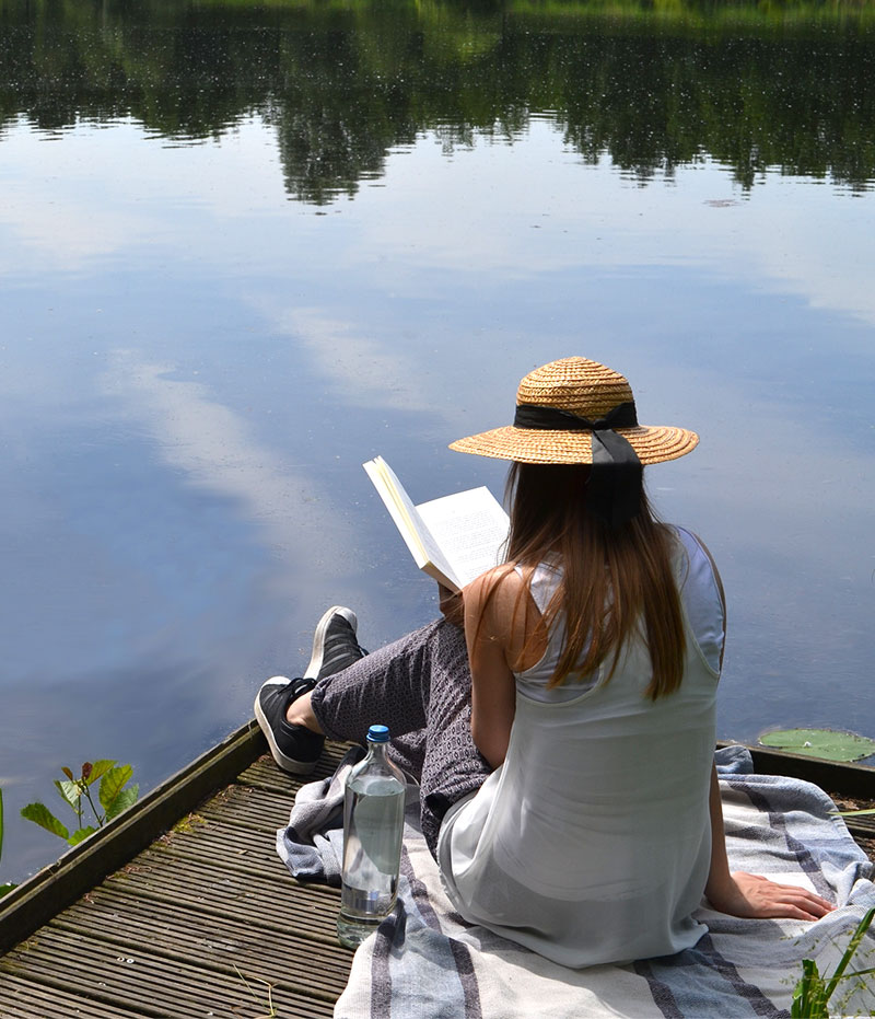 A woman is sitting on a lake and reading a book.